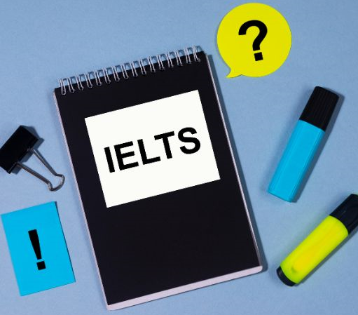 A black notepad with 'IELTS' written on it, surrounded by pens and stationery items.
