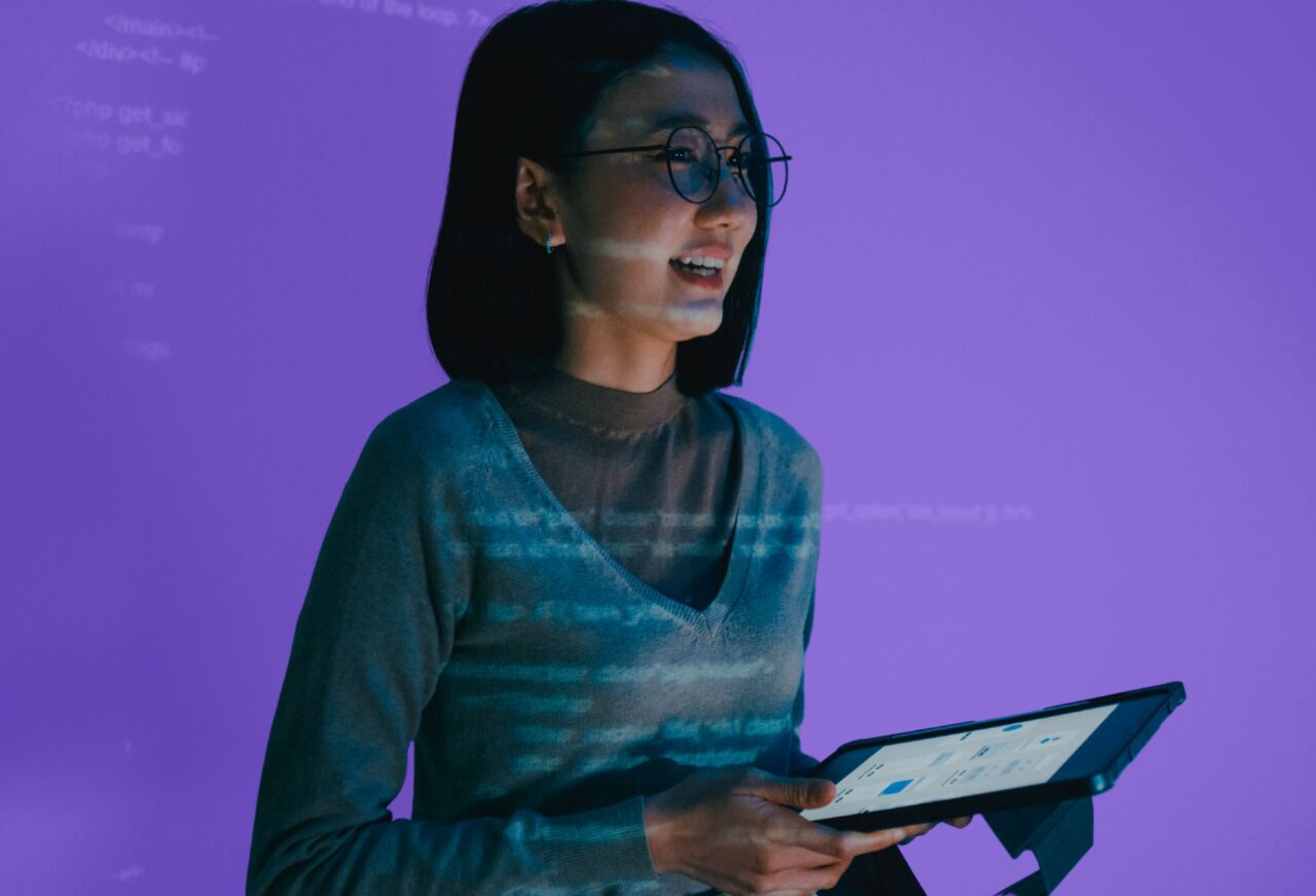 Student holding a tablet while reviewing digital technology interfaces and artificial intelligence concepts during a computer science education programme.