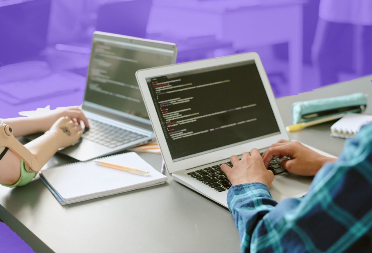 Students working together on laptops writing programming code and developing collaborative software projects during a computer science learning programme.