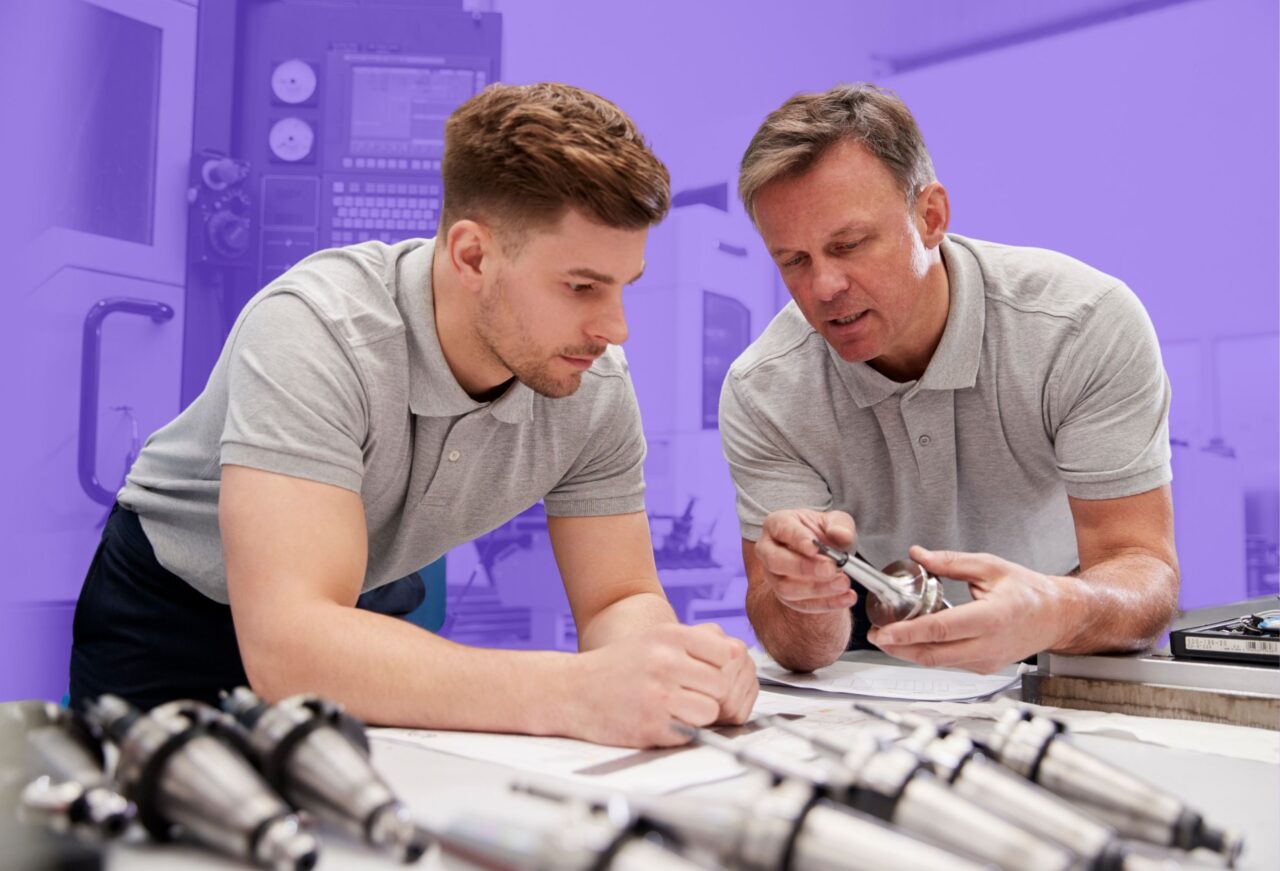 Engineering professional mentoring a student while reviewing mechanical components and discussing engineering design principles.